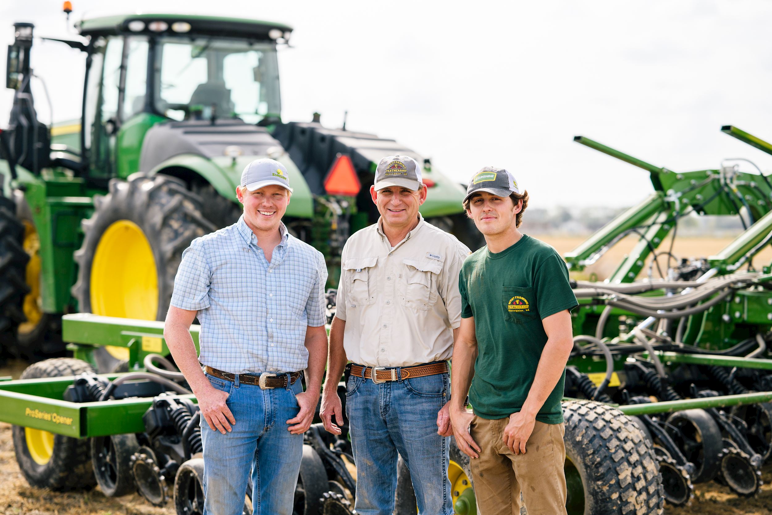 3 men smile in front of a John Deere tractor