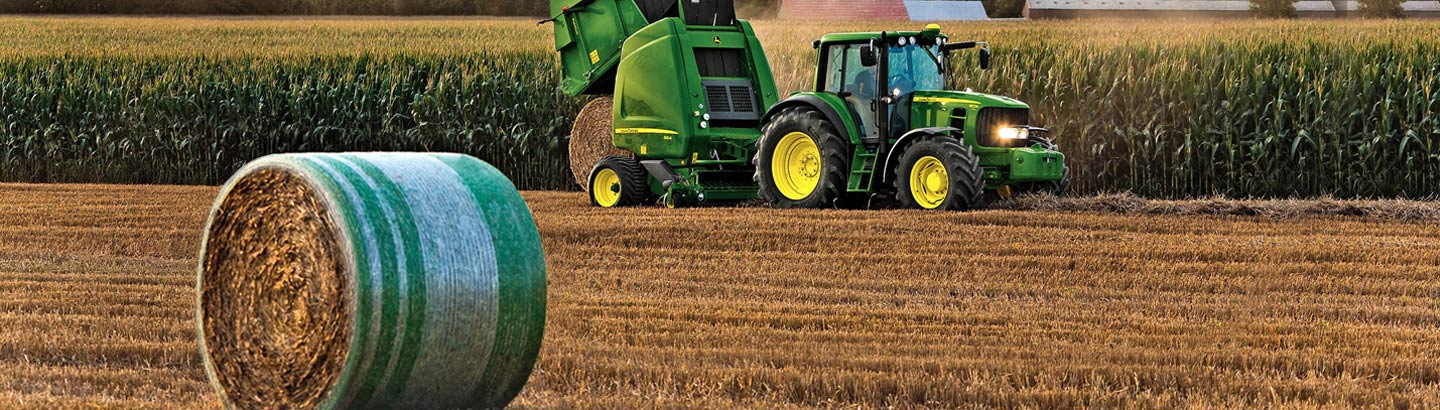 John Deere tractor and round baler in a hay field with a netwrapped round bale